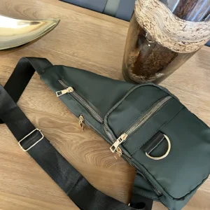 Bolso bandolera impermeable Spice verde oscuro con correa negra ajustable y detalles dorados, ideal para llevar esenciales.