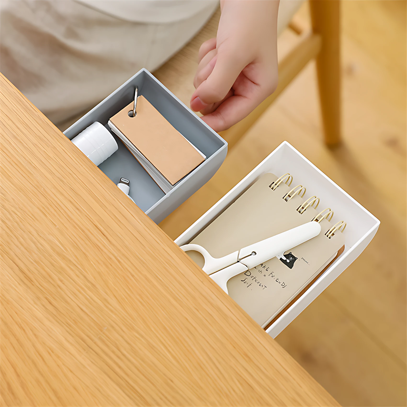 Cajón adhesivo gris para escritorio, con libretas y tijeras blancas.