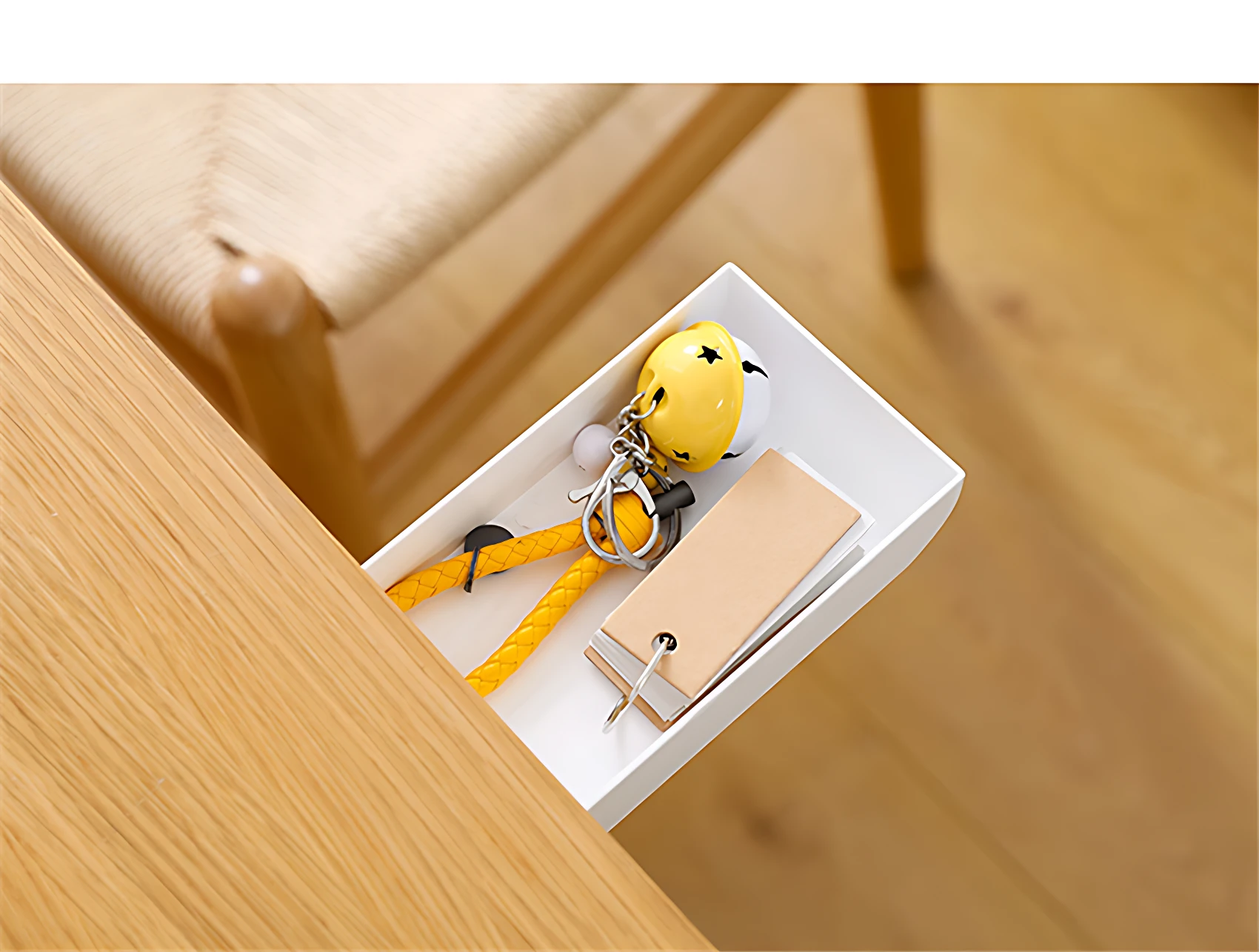 Cajón blanco adhesivo para escritorio con llavero amarillo, tarjetas de papel y silla de mimbre al fondo.