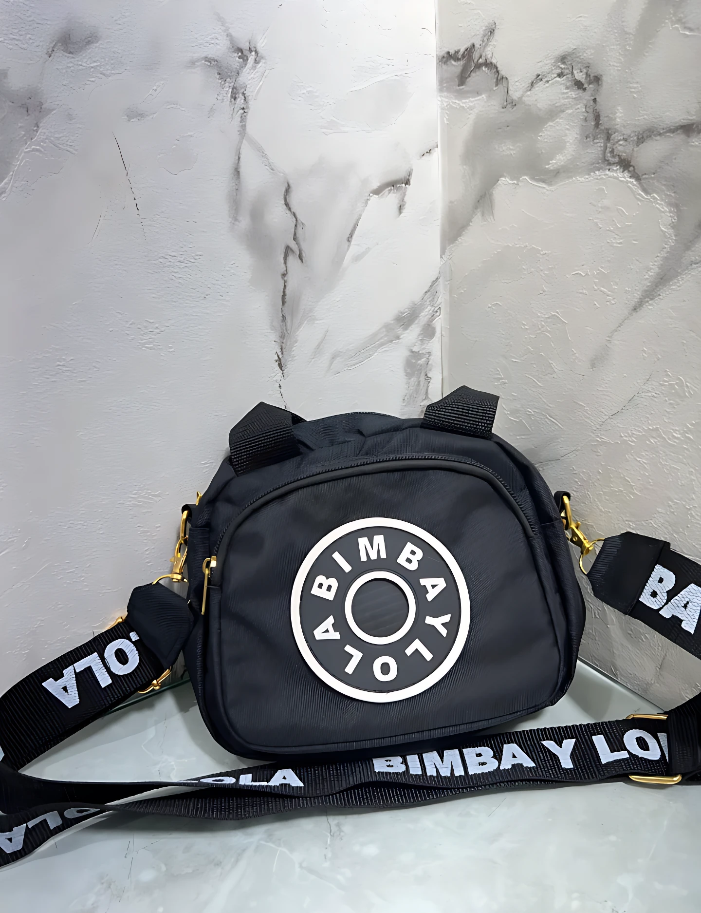 Carriel Bimba y Lola negro con logo circular blanco, correa estampada, ideal para llevar lo esencial.