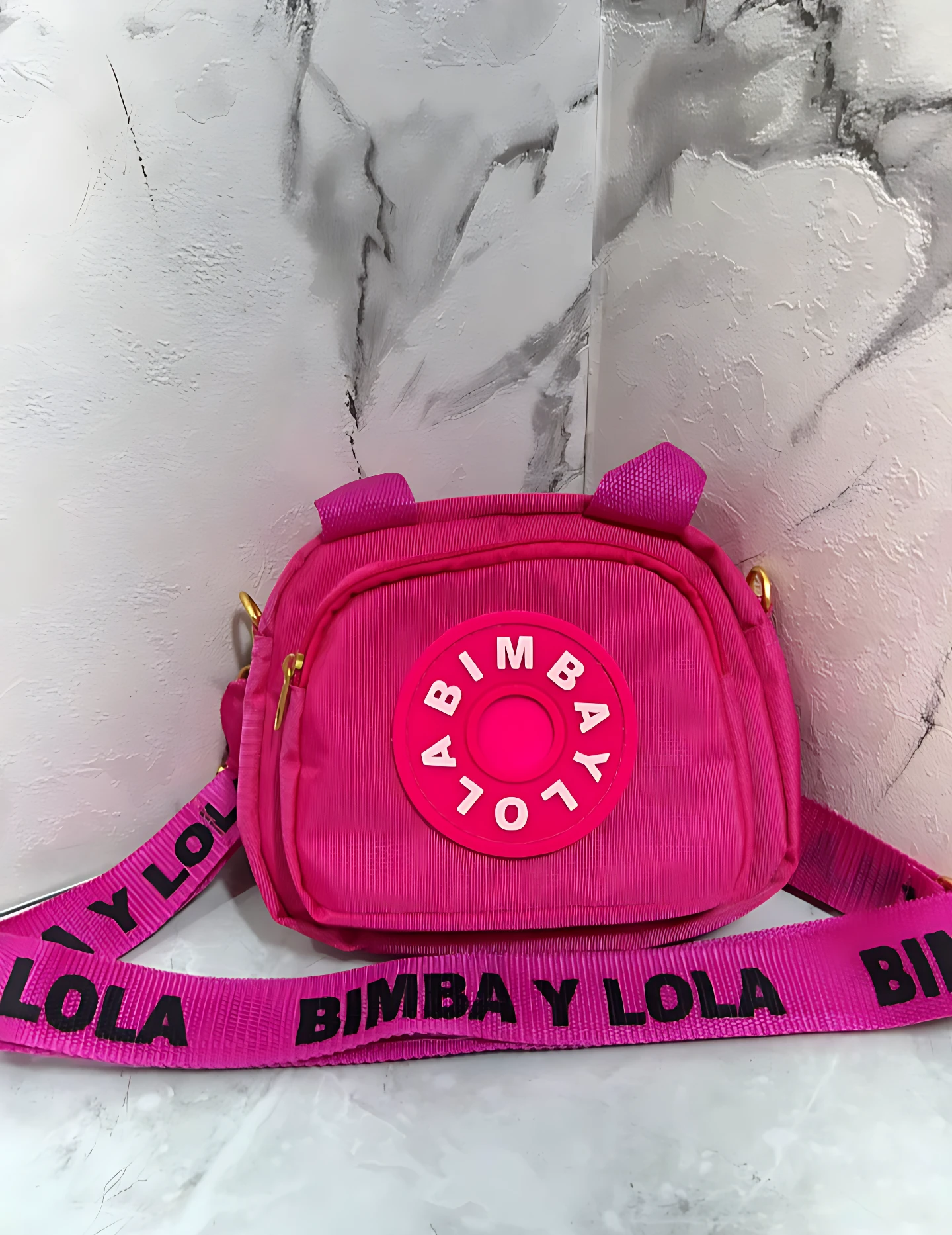 Carriel fucsia de corduroy Bimba y Lola, con logo circular y correa negra estampada.