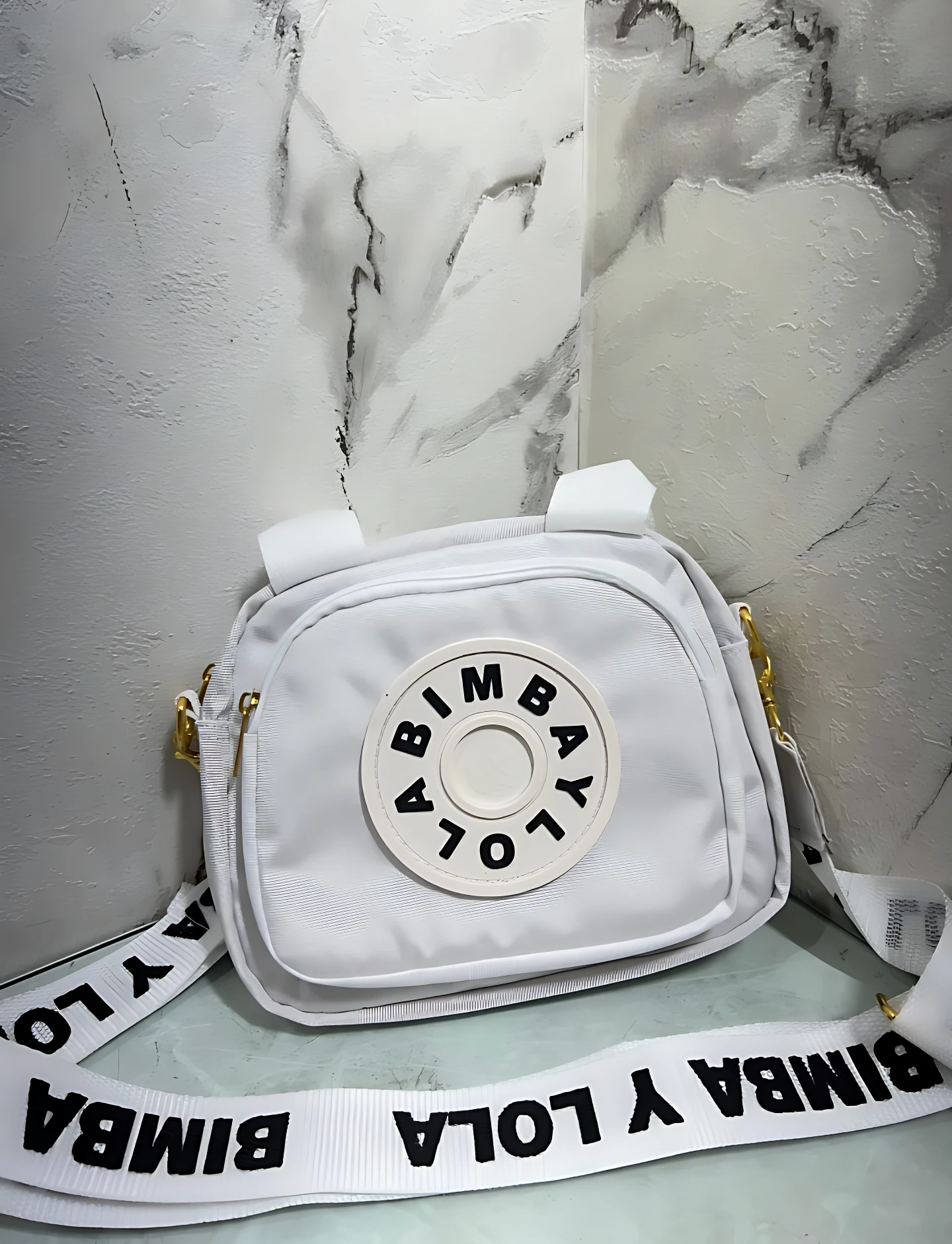 Carriel blanco Bimba y Lola con logo circular al frente y correa ancha con estampado de la marca.