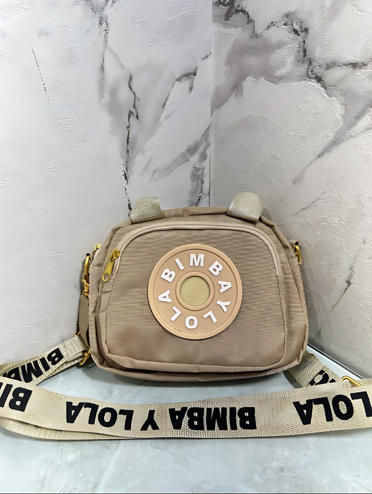 Carriel cruzado Bimba y Lola color beige con logo circular y correa con inscripción de la marca.