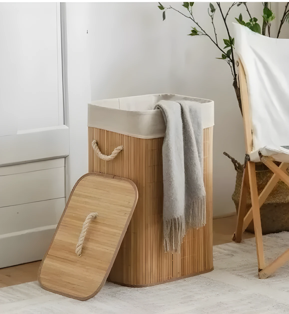 Cesta de ropa sucia de bambú con forro y tapa, con manta gris y silla de madera al lado.