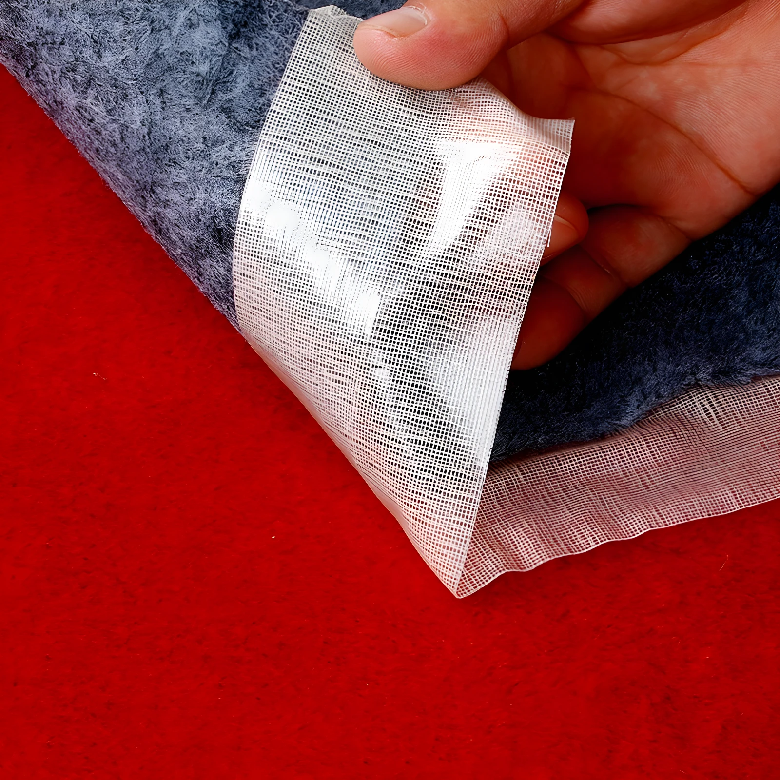 Cinta doble faz transparente multiuso desplegándose de alfombra gris sobre fondo rojo.
