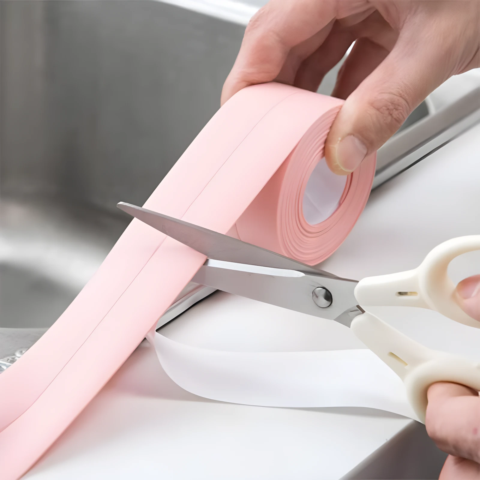 Cinta selladora adhesiva impermeable rosa cortándose con tijeras cerca de un lavaplatos.