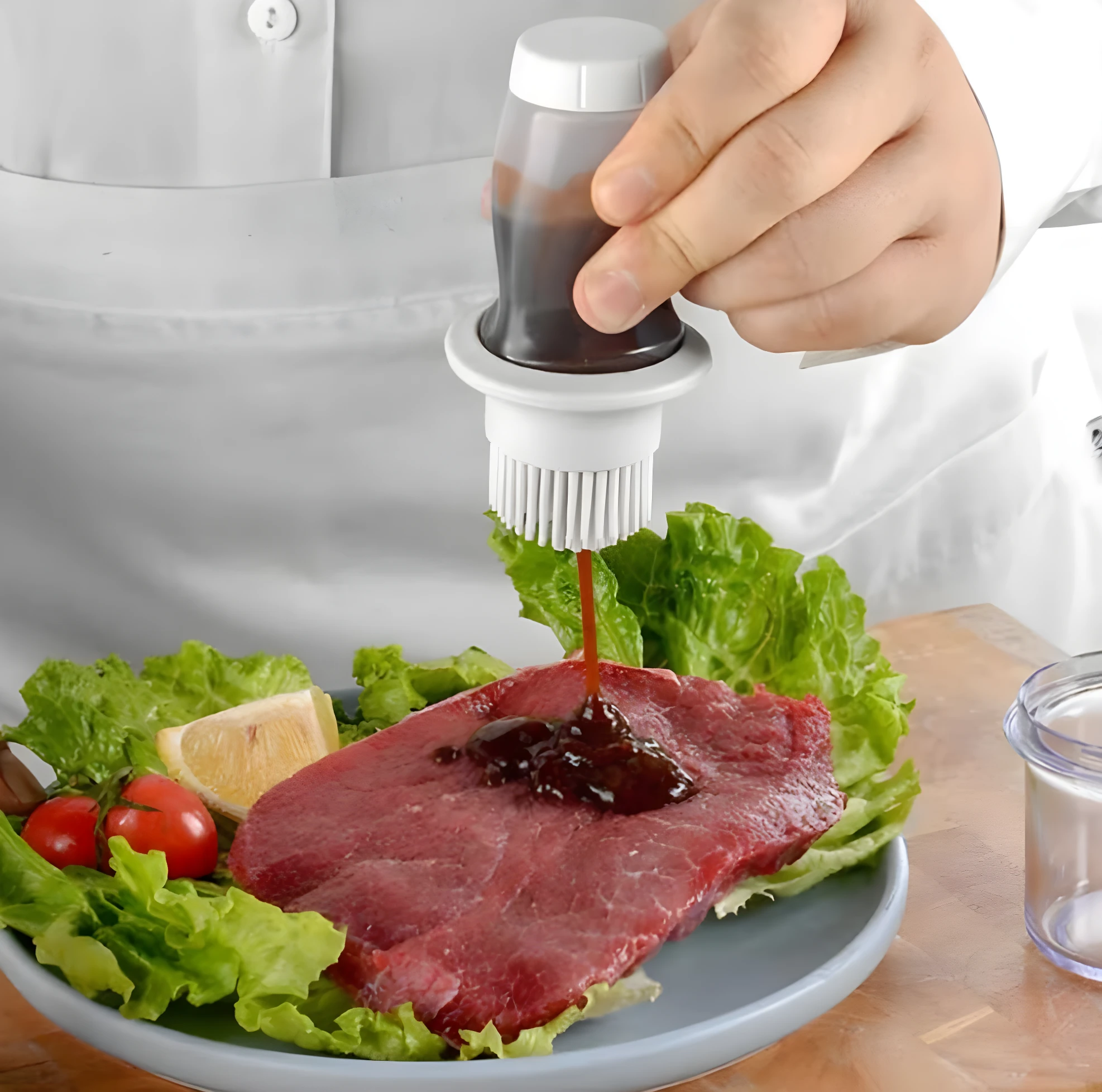 Dispensador de aceite con brocha aplicando salsa a bistec crudo servido con lechuga y tomate.