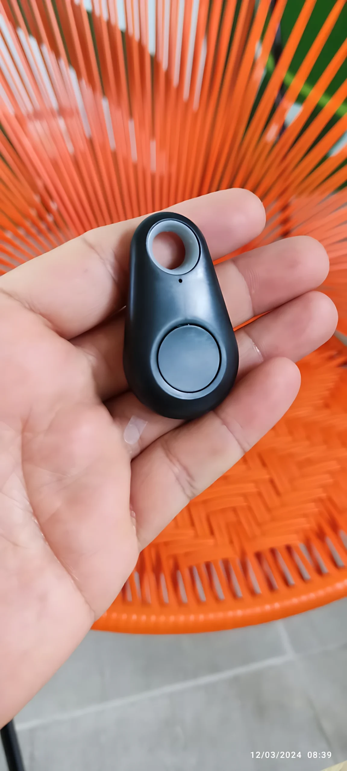 Extractor de jugos manual negro con localizador Bluetooth en mano, fondo naranja.