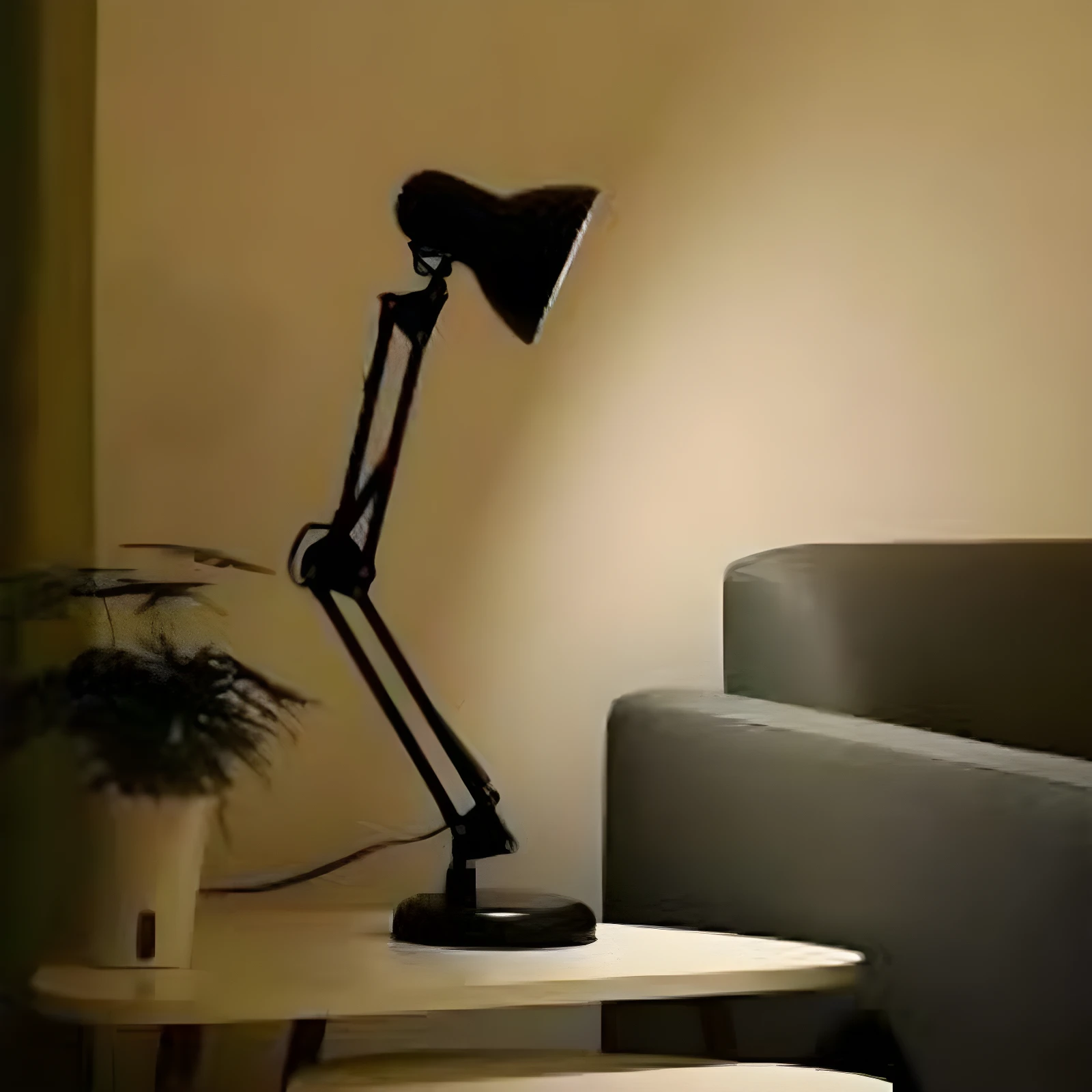 Lámpara de escritorio flexible color negro con brazo articulado, base redonda y cabezal orientable, ubicada sobre una mesa pequeña junto a una planta.