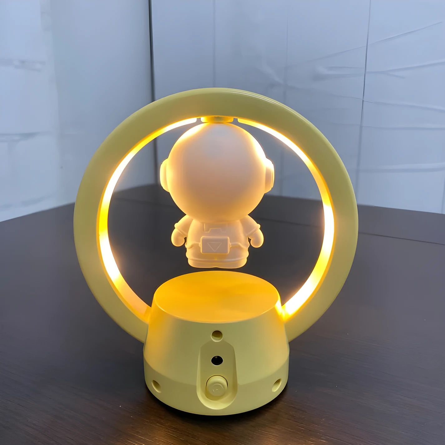 Lámpara de mesa LED amarilla con figura de astronauta flotante dentro de un aro luminoso.