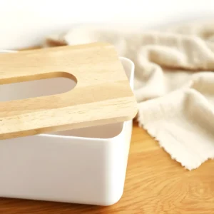 Dispensador blanco de pañuelos con tapa de bambú y apertura rectangular, sobre superficie de madera.