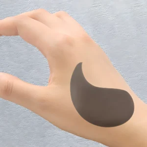 Parche negro revitalizante para ojeras y bolsas, posado sobre mano.
