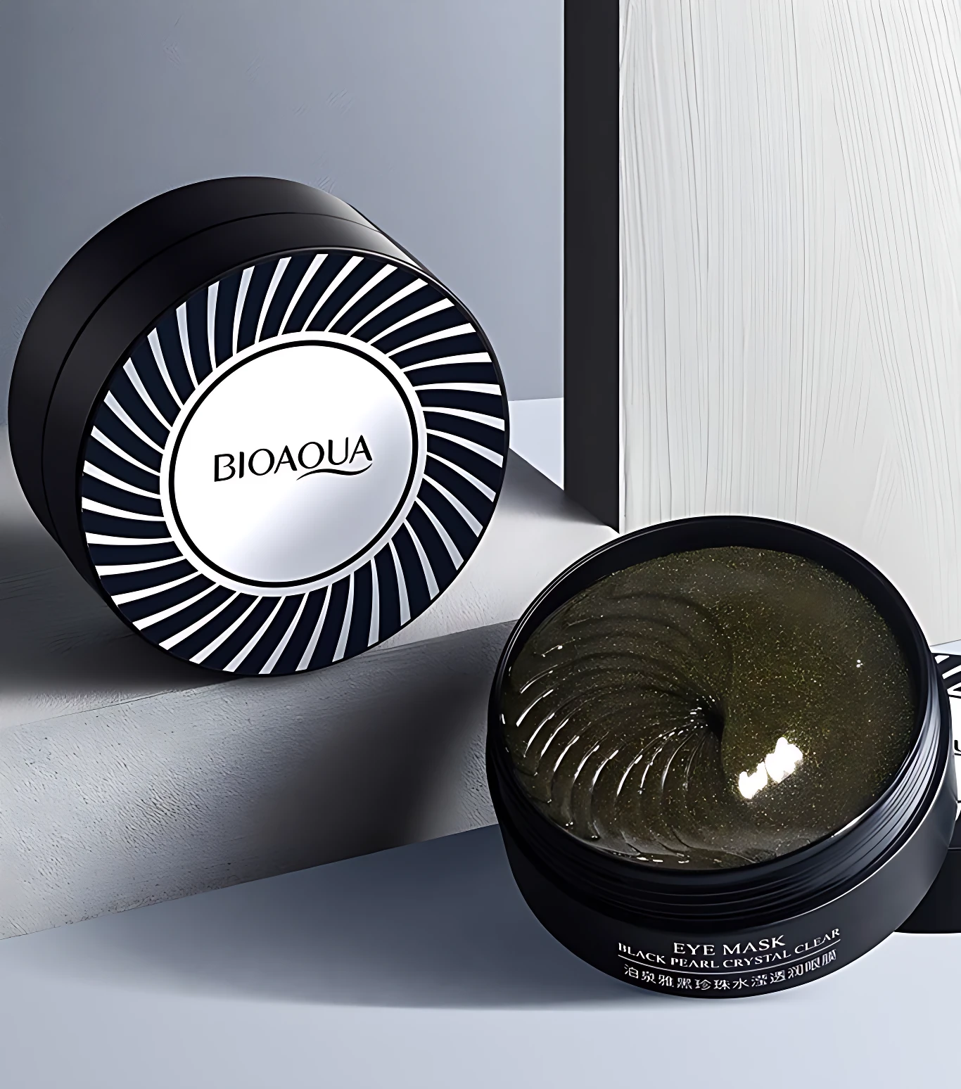 Dos recipientes de parches para ojeras BIOAQUA: uno cerrado negro con espiral plateado, otro abierto con parches negros y brillos, para revitalizar la mirada.