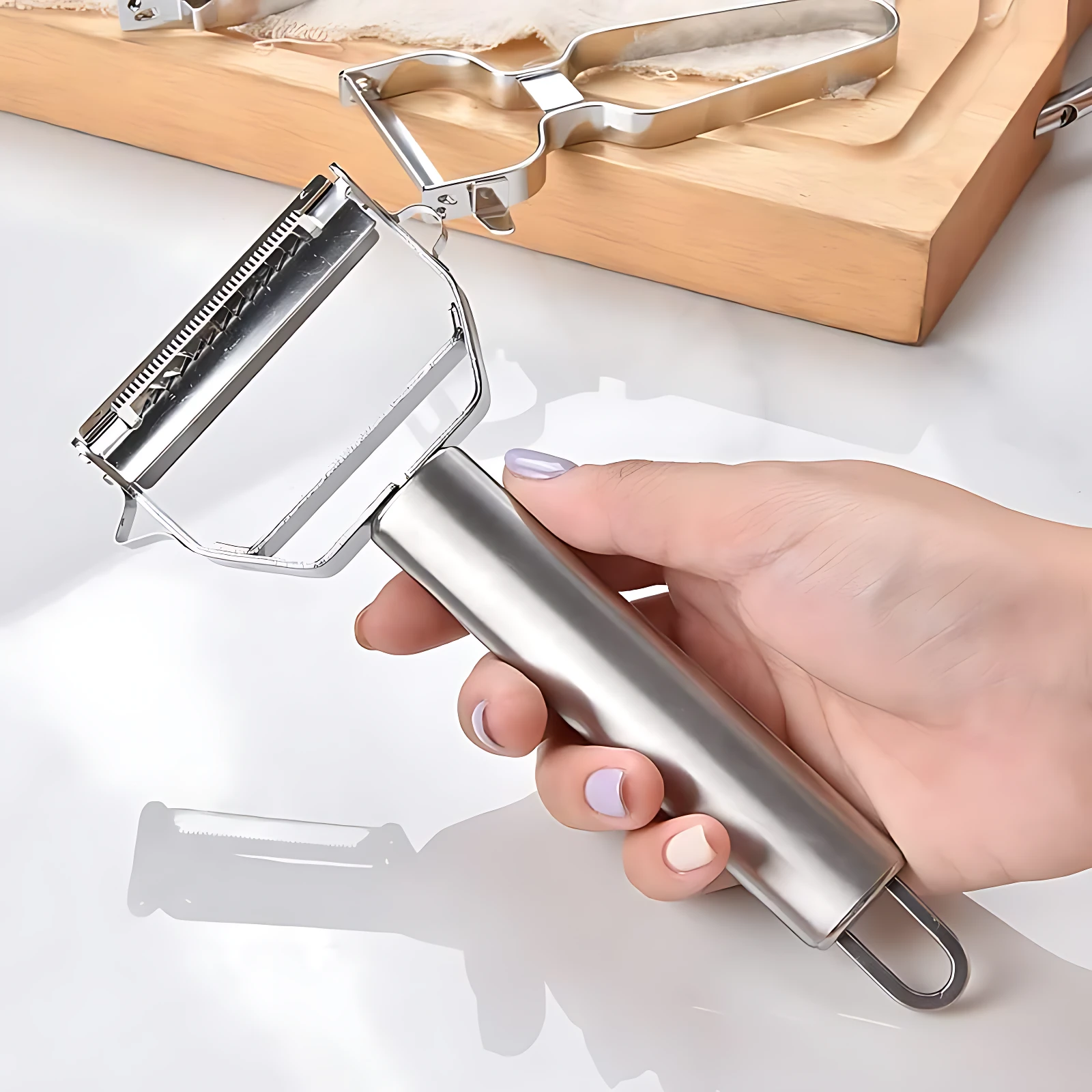 Pelador rallador multifuncional de acero inoxidable plateado en mano, ideal para verduras.