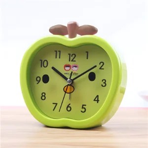 Reloj despertador verde en forma de manzana con manecillas negras y dos caritas sonrientes.