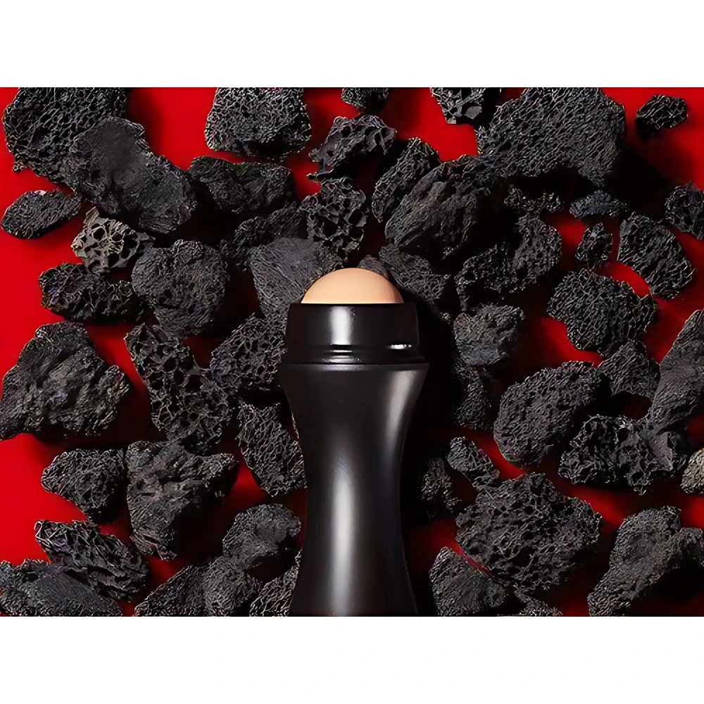 Roll-on quita grasa portátil negro con esfera beige, rodeado de rocas volcánicas negras sobre fondo rojo.