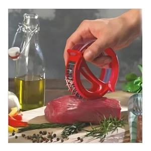 Ablandador de carne rojo con múltiples agujas sobre un trozo de res, con aceite de oliva y especias alrededor.