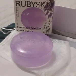 Jabón íntimo Rubyskin morado con niacinamida, en su empaque y sobre una malla, 100g.