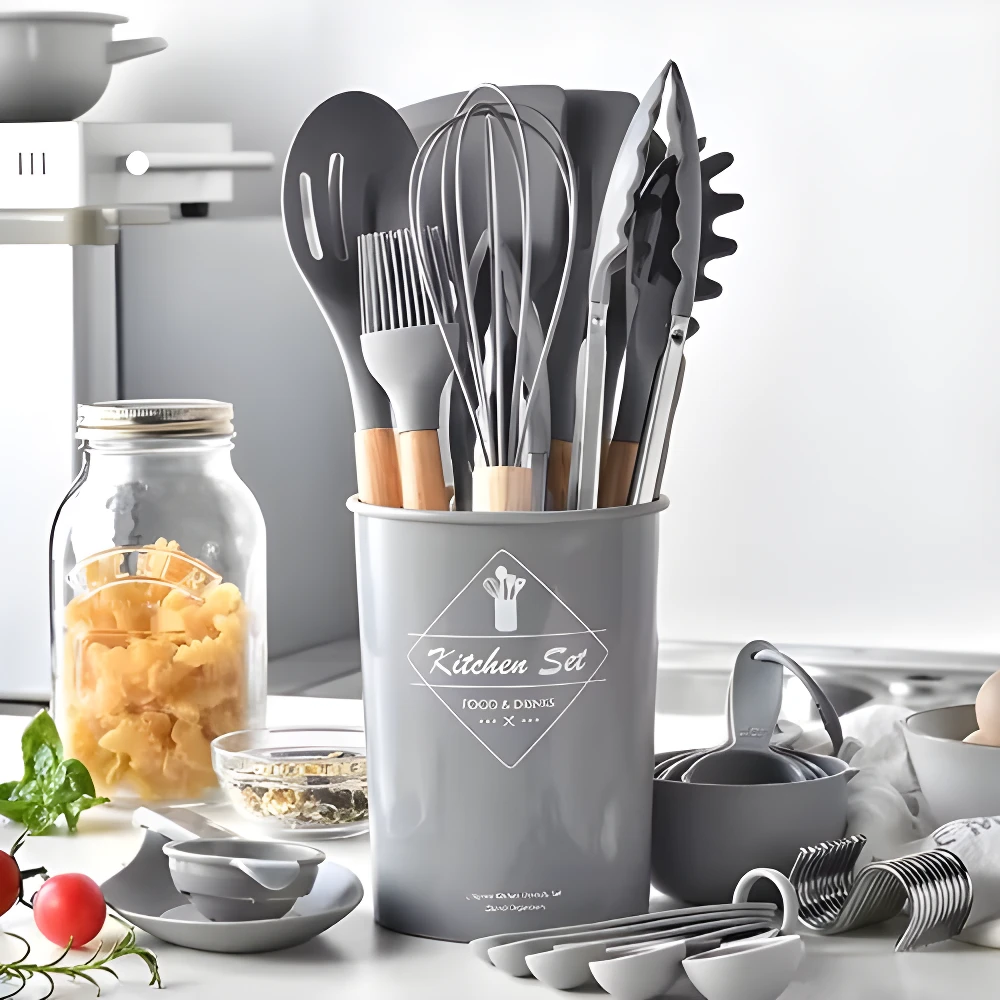 Set de 12 utensilios de cocina grises con mangos de madera, soporte, batidor y pinzas en primer plano.