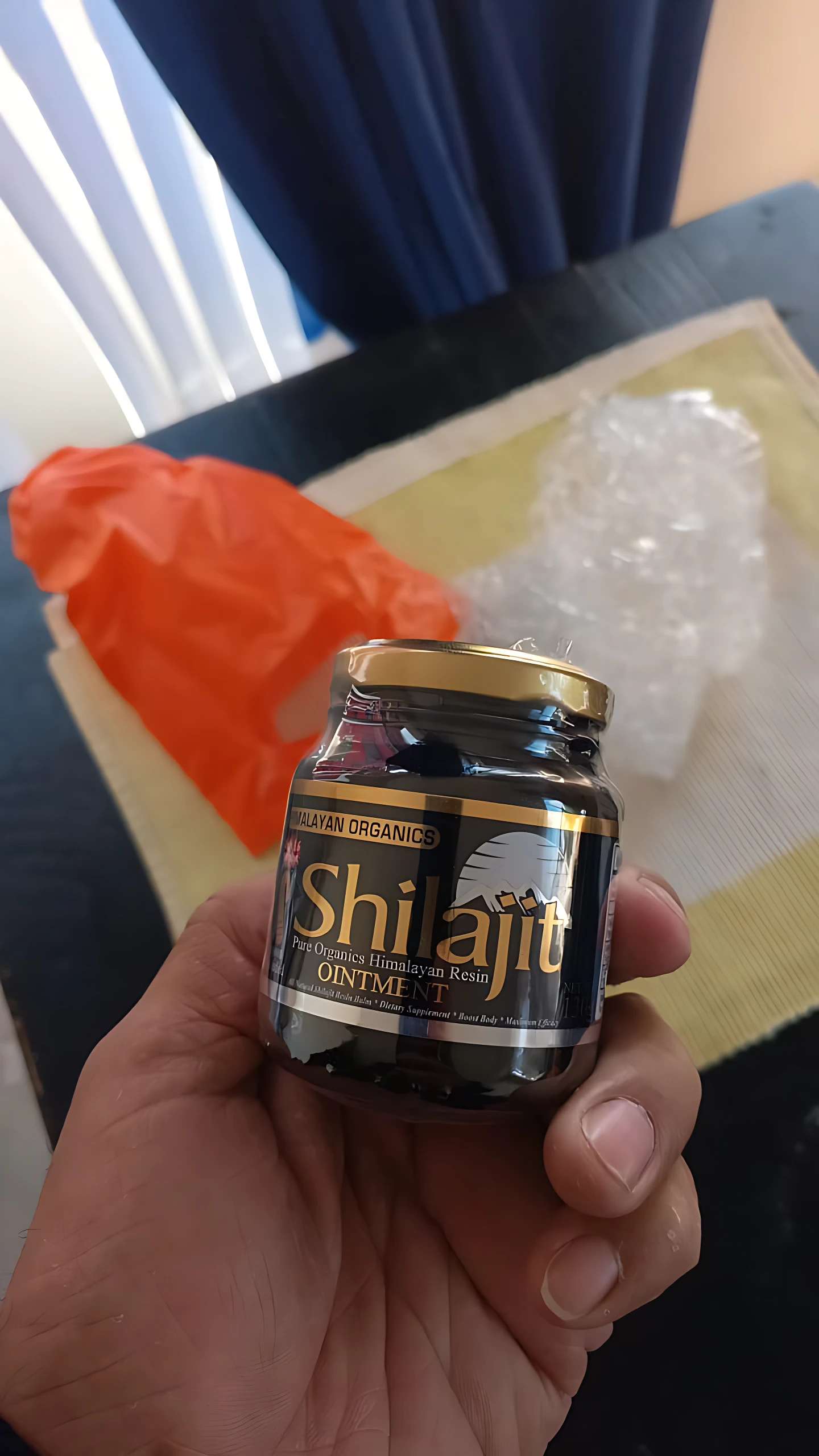 Mano sujetando frasco dorado y negro de Shilajit Resina Himalaya, 130g, para energía.