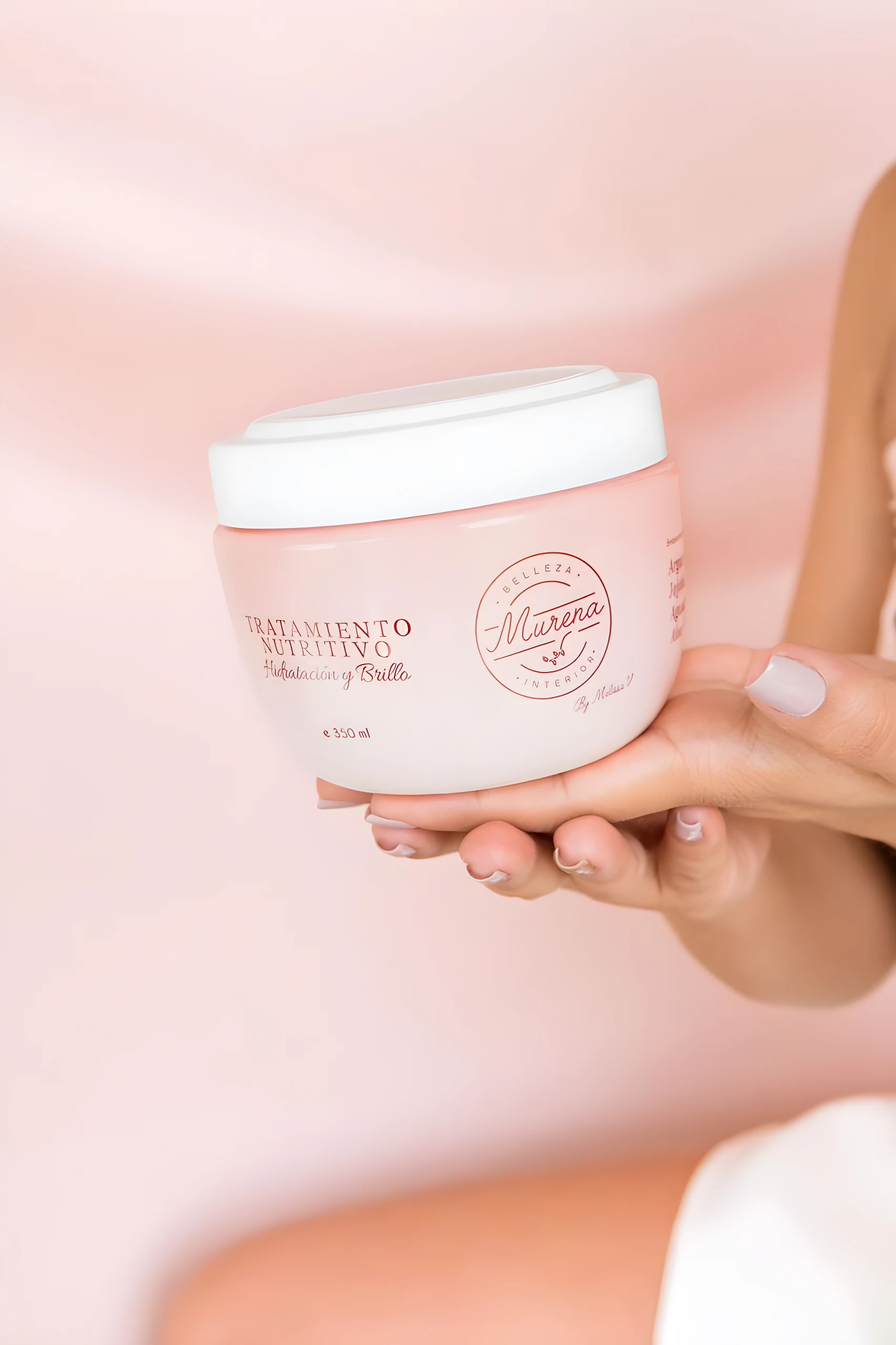 Crema capilar rosa Murena Tratamiento Nutritivo Hidratación Brillo 350 ml en manos con uñas pintadas.
